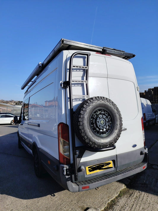 White van with a spare tire mounted on the back, parked on a concrete surface with a clear blue sky.